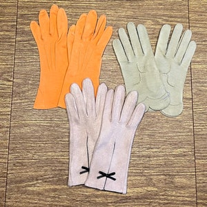 May include: Four pairs of gloves, two pairs are orange and two pairs are beige. The beige gloves have a black bow detail.