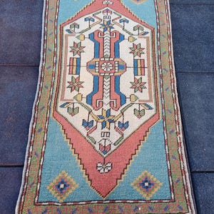 Könnte beinhalten: Ein Vintage-Teppich mit einem geometrischen Muster in Blautönen, Rot, Gelb und Weiß. Der Teppich hat einen Fransenrand und ist aus Wolle.