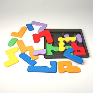 May include: A colourful puzzle game featuring geometric shapes in red, orange, yellow, green, blue, and purple. The puzzle pieces are scattered around a black tray with matching cutouts. The game is designed for spatial reasoning and problem-solving.