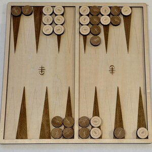 May include: A wooden backgammon board with dark brown and light brown triangular markings. The board is set with light and dark wooden game pieces. The game board is rectangular and has a light wood finish.