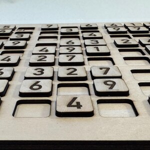 May include: A wooden game board with a grid of squares, each containing a number from 1 to 9. The board is made of light brown wood and has a natural finish.