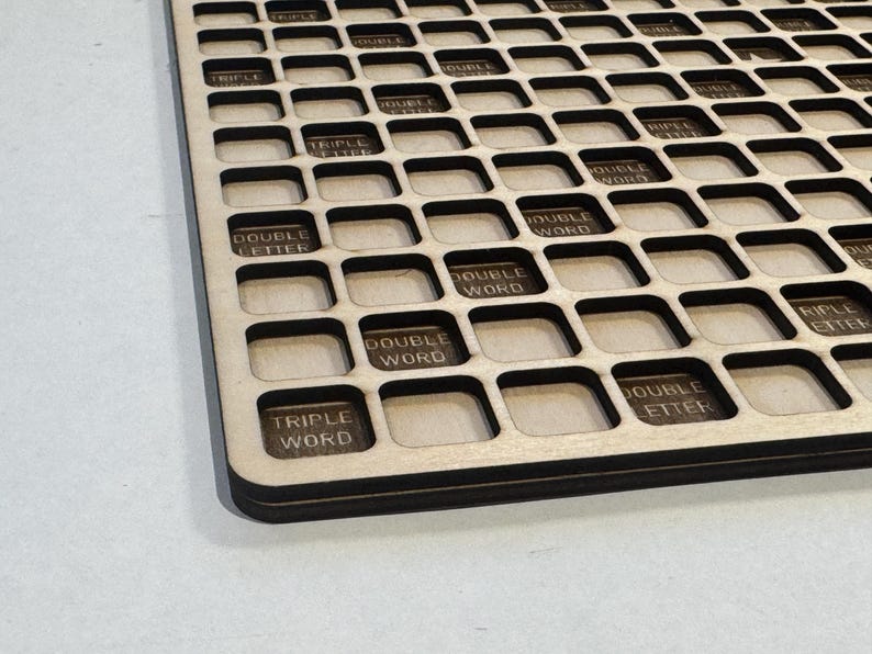 May include: A wooden game board with a grid of square spaces. Some squares are labeled with text like "DOUBLE WORD" and "TRIPLE WORD". The board has a dark border and is made of light-colored wood.