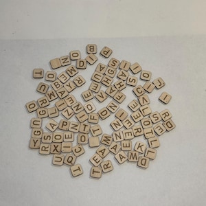 May include: A collection of small, square wooden tiles, each etched with a single letter or number. The tiles are scattered across a white surface, creating a random assortment of characters. The natural wood color provides a neutral backdrop.