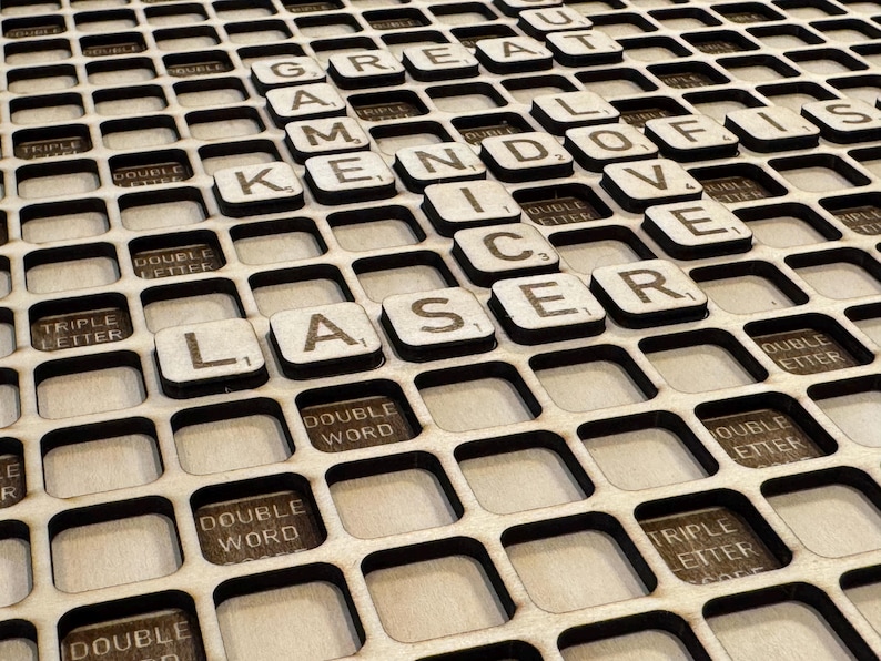 May include: Wooden game board with laser-cut grid and Scrabble tiles spelling "GREAT GAMES, KENDO, ICE, LASER, LOVE, IS". The board features spaces for double and triple letter/word scores.