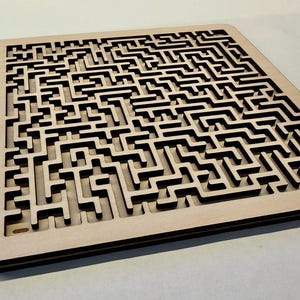 Pode incluir: Um quebra-cabeça de labirinto de madeira com um design complexo. O labirinto é cortado de madeira clara, com sombras escuras criando contraste nos caminhos. O quebra-cabeça é retangular e repousa sobre uma superfície neutra.