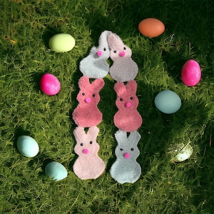 May include: A knitted scarf with a pattern of pink and white bunny rabbits. The scarf is surrounded by pastel colored Easter eggs.