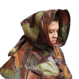 May include: A brown leather hooded cape with a patchwork design. The cape is made of different shades of brown, green, and tan leather. The hood is lined with brown leather and has a drawstring closure.