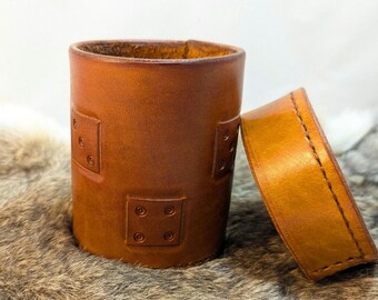May include: A brown leather dice rolling tower with a dice pattern embossed on the side. The tower is open and the lid is laying next to it.