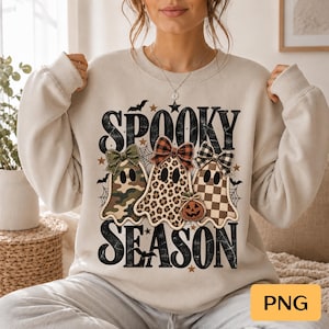Może przedstawiać: Beżowa bluza z okrągłym dekoltem i czarnym napisem SPOOKY SEASON. Wzór przedstawia trzy duszki z kokardkami: jeden w kamuflaż, drugi w panterkę, a trzeci w kratkę, oraz małą pomarańczową dynię.