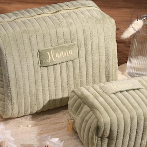 Op de afbeelding: Twee saliegroene corduroy cosmetische tassen met gouden ritsen. De grotere tas heeft een rechthoekige vorm en de kleinere tas is rechthoekig. Beide tassen hebben de naam "Hanna" geborduurd op een rechthoekige patch.