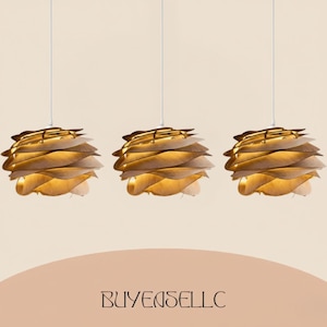 May include: Three pendant lights with a layered, leaf-like design. The lampshades are made of light-colored wood, with a warm glow emanating from within. Each light hangs from a white cord against a neutral background. The text "BUYENSELLC" is at the bottom.