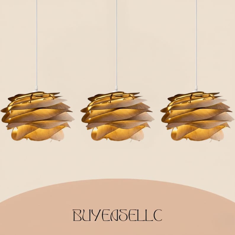 May include: Three pendant lights with a layered, leaf-like design. The lampshades are made of light-colored wood, with a warm glow emanating from within. Each light hangs from a white cord against a neutral background. The text "BUYENSELLC" is at the bottom.