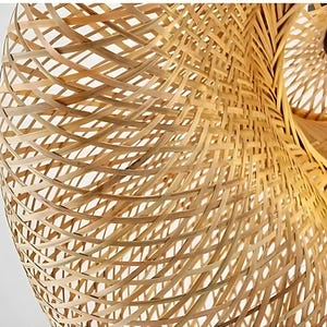 May include: Close-up of a woven bamboo lampshade. The natural-toned shade features a complex, open weave pattern, creating a textured surface. The design allows light to filter through, creating a warm, inviting glow. The lampshade is a decorative lighting fixture.