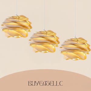 May include: Three modern pendant lights with a layered, petal-like design. The lights are a warm gold color, with white accents, and hang from white cords against a neutral background. The text "BUYENSELLC" is at the bottom.