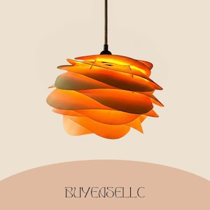 May include: A modern, layered pendant light fixture with a warm orange and yellow color scheme. The light has a unique, petal-like design, suspended from a brown cord. The text "BUYENSELLC" is at the bottom.