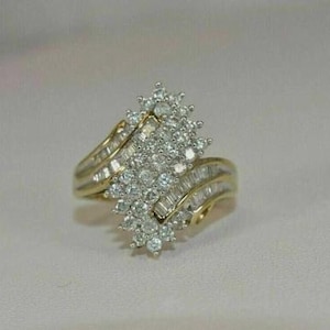 May include: A gold-toned ring with a cluster of small, round diamonds and baguette-cut diamonds. The ring has a multi-layered band design, with the diamonds arranged in a floral or starburst pattern.