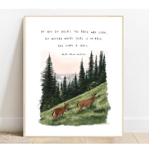 May include: A framed art print featuring a watercolor illustration of two deer on a grassy hillside with evergreen trees. The print includes the quote "DO NOT GO WHERE THE PATH MAY LEAD, GO INSTEAD WHERE THERE IS NO PATH AND LEAVE A TRAIL." by Ralph Waldo Emerson.
