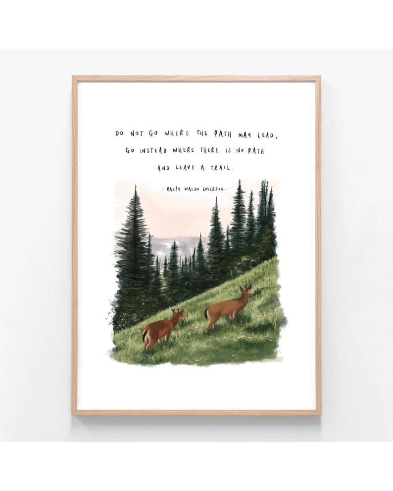 May include: A framed art print featuring a landscape scene with two deer grazing on a grassy hill. The artwork includes a forest of tall evergreen trees and a quote by Ralph Waldo Emerson: "Do not go where the path may lead, go instead where there is no path and leave a trail."