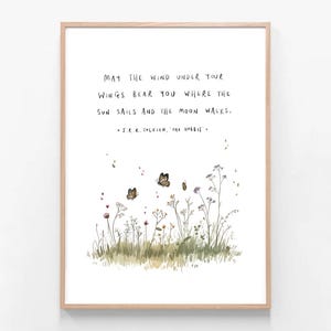 May include: A framed art print with a quote from J.R.R. Tolkien's "The Hobbit." The quote, in black handwritten font, reads "May the wind under your wings bear you where the sun sails and the moon walks." Features a watercolour illustration of butterflies and wildflowers.