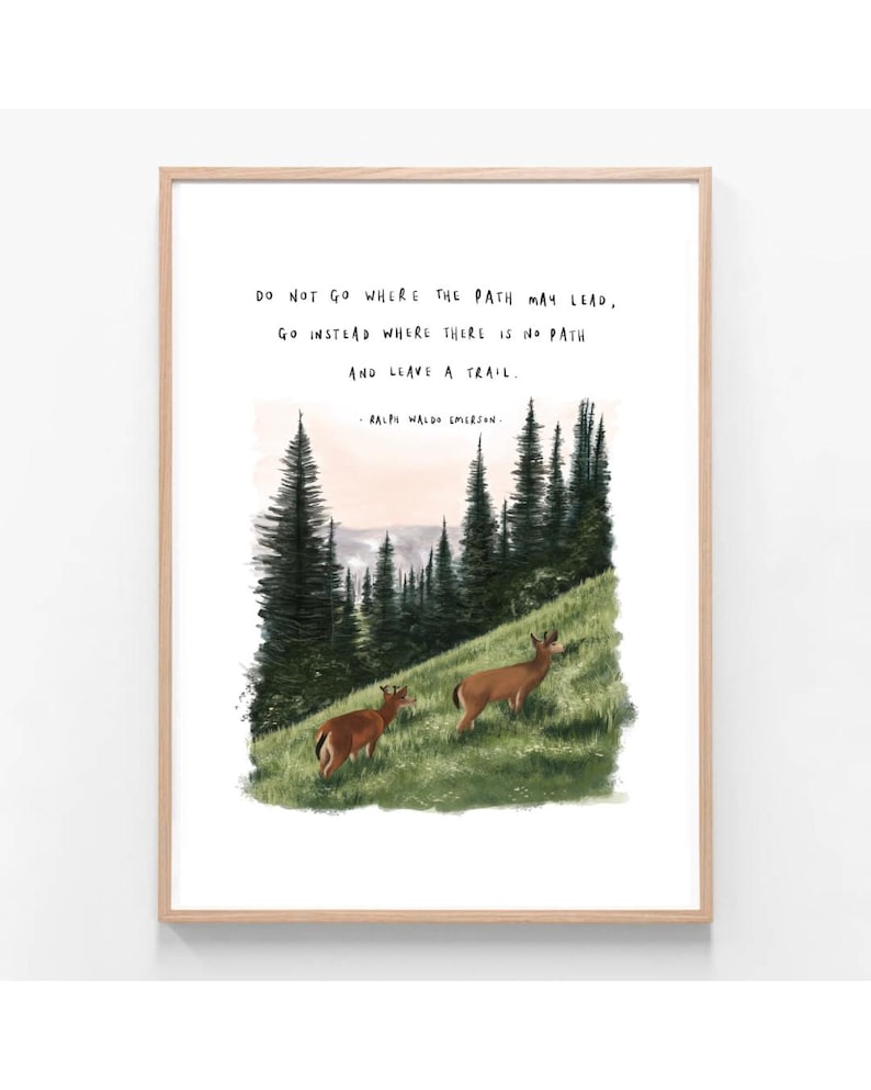 May include: A framed art print featuring a landscape scene with two deer grazing on a grassy hill. The artwork includes tall evergreen trees and a quote by Ralph Waldo Emerson: "Do not go where the path may lead, go instead where there is no path and leave a trail."