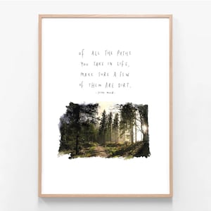 May include: A framed print with a forest scene and a dirt path. The artwork displays the quote, "Of all the paths you take in life, make sure a few of them are dirt." The quote is attributed to John Muir. The frame is a light wood colour.