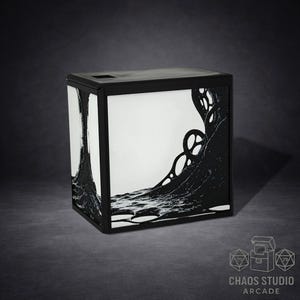 May include: Black and white box with a unique design. The box has a black frame and features a stylized black design on a white background. The design appears to be an abstract representation of a wave or flowing form. The box has a square shape.