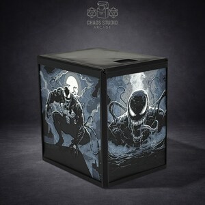 May include: Black box featuring Venom artwork. The box has a black frame and illuminated panels with illustrations of the Marvel Comics character. The top of the box has the text "Chaos Studio Arcade".