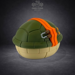 May include: A Teenage Mutant Ninja Turtle-themed figurine. The figurine is green with an orange sash, brown weapon holders, and a light yellow base. The top of the figurine is a turtle shell design. The text "Chaos Studio Arcade" is visible.