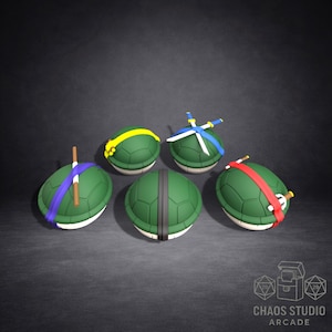 May include: Five green turtle shell-shaped objects with different colored headbands and weapons. The headbands are yellow, blue, and red. The weapons include a staff, swords, and a pair of sais. The objects are on a dark gray background. The text "CHAOS STUDIO ARCADE" is in the bottom right corner.