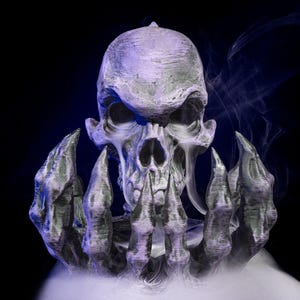 May include: A detailed, gray skull with sharp teeth and a textured surface, held by skeletal hands. The image is set against a dark background with wisps of white smoke, creating a spooky, Halloween-themed aesthetic.