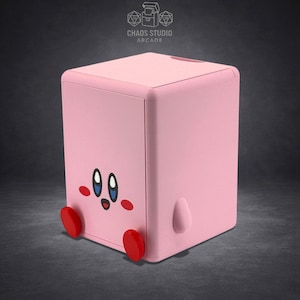 May include: A pink, cube-shaped storage box featuring a cartoon character face with large eyes, red cheeks, and red feet. The box has a small, rounded handle on the side and the text "Chaos Studio Arcade" at the top.