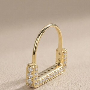 May include: A gold-colored earring with a square base and a curved top. The square base is encrusted with small, clear gemstones. The earring is designed to be worn through a pierced ear.