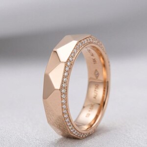 May include: Rose gold ring with a geometric design. The ring features a faceted exterior and a band lined with small, sparkling diamonds. The interior of the band has engraved markings.