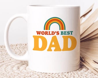 May include: White ceramic mug with a large handle, featuring the text "WORLD'S BEST DAD" in orange and a rainbow design. The mug is a standard size and shape, suitable for hot or cold beverages.