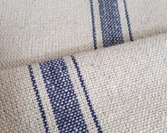 May include: Close-up of a natural linen fabric with woven blue stripes. The fabric has a textured appearance and a neutral color palette, suitable for various home decor projects. The stripes are evenly spaced and add a classic touch.