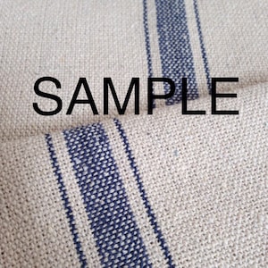 May include: A close-up of a natural linen fabric with two wide blue stripes running vertically. The fabric has a textured, woven appearance. The word "SAMPLE" is printed in black across the fabric.