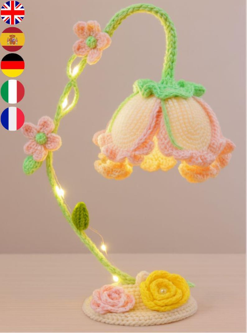 May include: A handcrafted crochet flower lamp with a light green stem and a cream-colored base. The lamp features a large flower-shaped shade in shades of yellow and peach, with small LED lights. The base has pink and yellow crochet flowers.