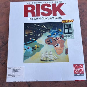 May include: A boxed computer game titled "RISK: The World Conquest Game." The box is white with red text and a colorful illustration of a world map with military elements. The Microsoft Windows logo and Virgin Games logo are visible.
