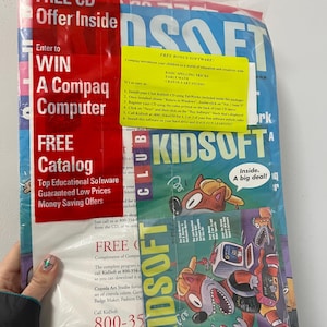 May include: A sealed plastic package containing a KidSoft Club magazine and a CD. The magazine features cartoon illustrations and the text "KIDSOFT CLUB." The package also includes offers for a Compaq computer and free software.
