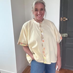 Può includere: Una camicia gialla con colletto e bordino a stampa floreale. La camicia ha una vestibilità rilassata e maniche corte.