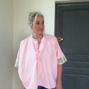 May include: A pink button-up shirt with floral print on the cuffs. The shirt has a relaxed fit and a collar.