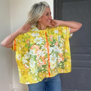 May include: A yellow floral print shirt with orange trim and a button closure. The shirt has a relaxed fit and short sleeves.