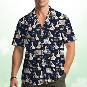 Puede incluir: Camisa azul marino de manga corta con un estampado repetido de gansos de dibujos animados con batas de laboratorio, gafas y vasos de precipitados. Los gansos se representan en varios entornos de laboratorio, con una tabla periódica visible. La camisa tiene un cuello clásico.