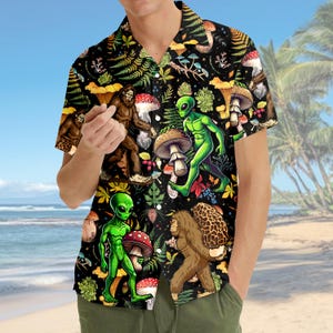May include: Black button-up shirt with a vibrant, whimsical pattern featuring green aliens, brown Bigfoot creatures, and colorful mushrooms. The shirt has short sleeves and a classic collar, perfect for a casual, eye-catching look.