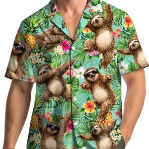 May include: Short-sleeved shirt with a tropical design. The shirt features cartoon sloths wearing sunglasses and posing amongst pineapples, flowers, and green foliage. The background is light blue.