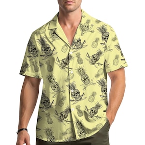 Può includere: Camicia giallo chiaro a maniche corte con un motivo ripetuto di ananas a forma di teschio nero e spade incrociate. La camicia ha un colletto classico ed è realizzata in un tessuto leggero.