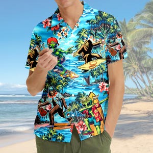 Op de afbeelding: Korte mouwen shirt met een tropisch ontwerp. Het blauwe shirt heeft illustraties van aliens en Bigfoot die surfen en muziek maken, tegen een achtergrond van palmbomen en bloemen. Het heeft een klassieke kraag en een relaxte pasvorm.