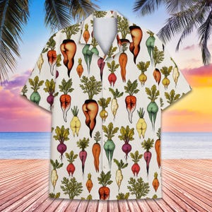 May include: White short-sleeved shirt featuring a repeating pattern of cartoon root vegetables with human-like features. The vegetables are in various colours and skin tones. The background shows a beach scene with palm trees and a sunset.
