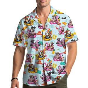 Puede incluir: Camisa azul claro de manga corta con un estampado repetido de monos de dibujos animados relajándose en flamencos y patos inflables. El diseño incluye gafas de sol, cócteles y accesorios de playa. La camisa tiene un cuello clásico.