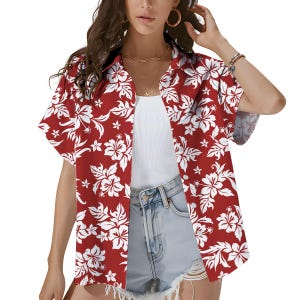 May include: Red Hawaiian shirt featuring a white floral design. The short-sleeved shirt has a button-down front and a classic collar. The shirt is open, revealing a white vest top and denim shorts.